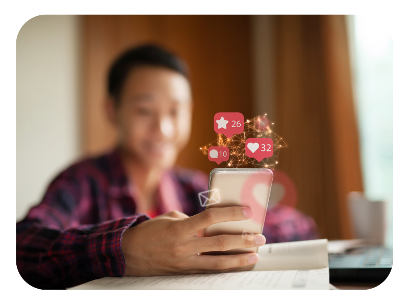 A man smiling at his phone with graphics coming out of the top of a like, comment and star metrics, representing social media engagement.