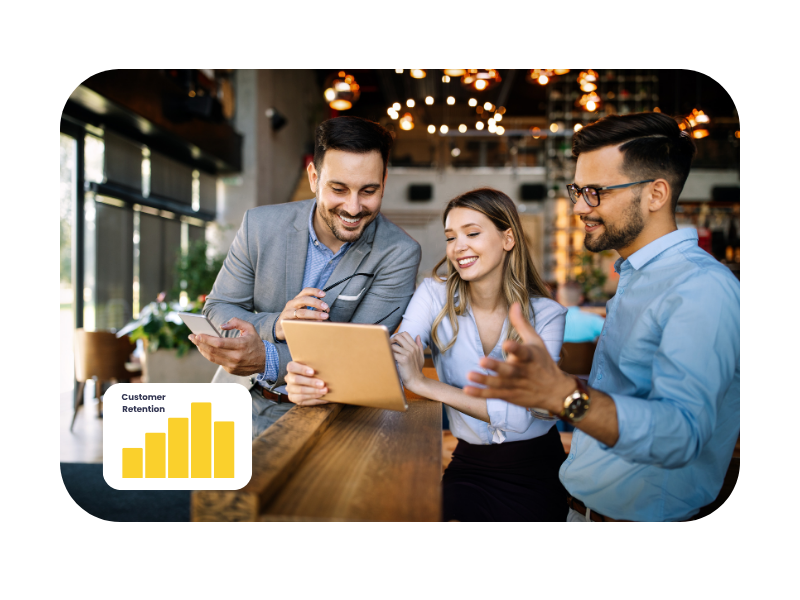 Three young professionals engaged in a lively discussion around a tablet in a modern workspace, with a "Customer Retention" chart displayed, highlighting practical learning and collaboration in marketing apprenticeships.