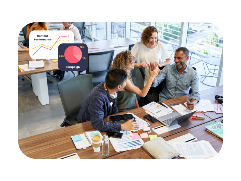 Group of professionals celebrating teamwork around a table with charts and laptops—illustrating collaborative learning in digital marketing apprenticeships.