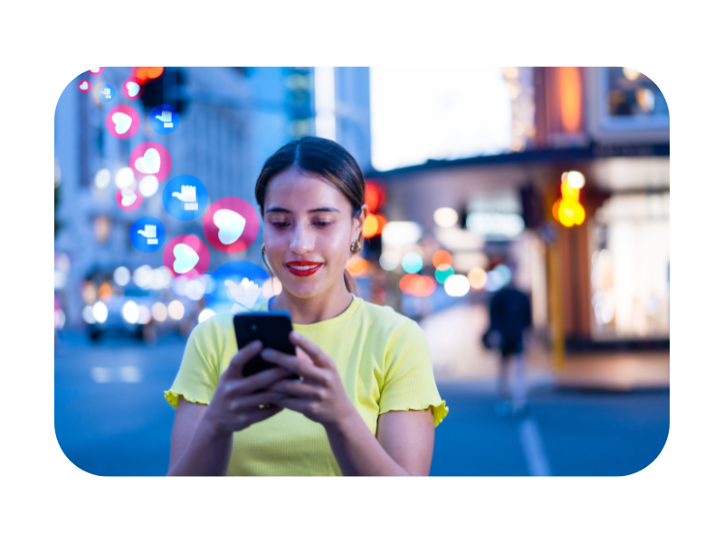 Young woman using her smartphone in the city at night with floating likes and hearts, representing engagement in social media.